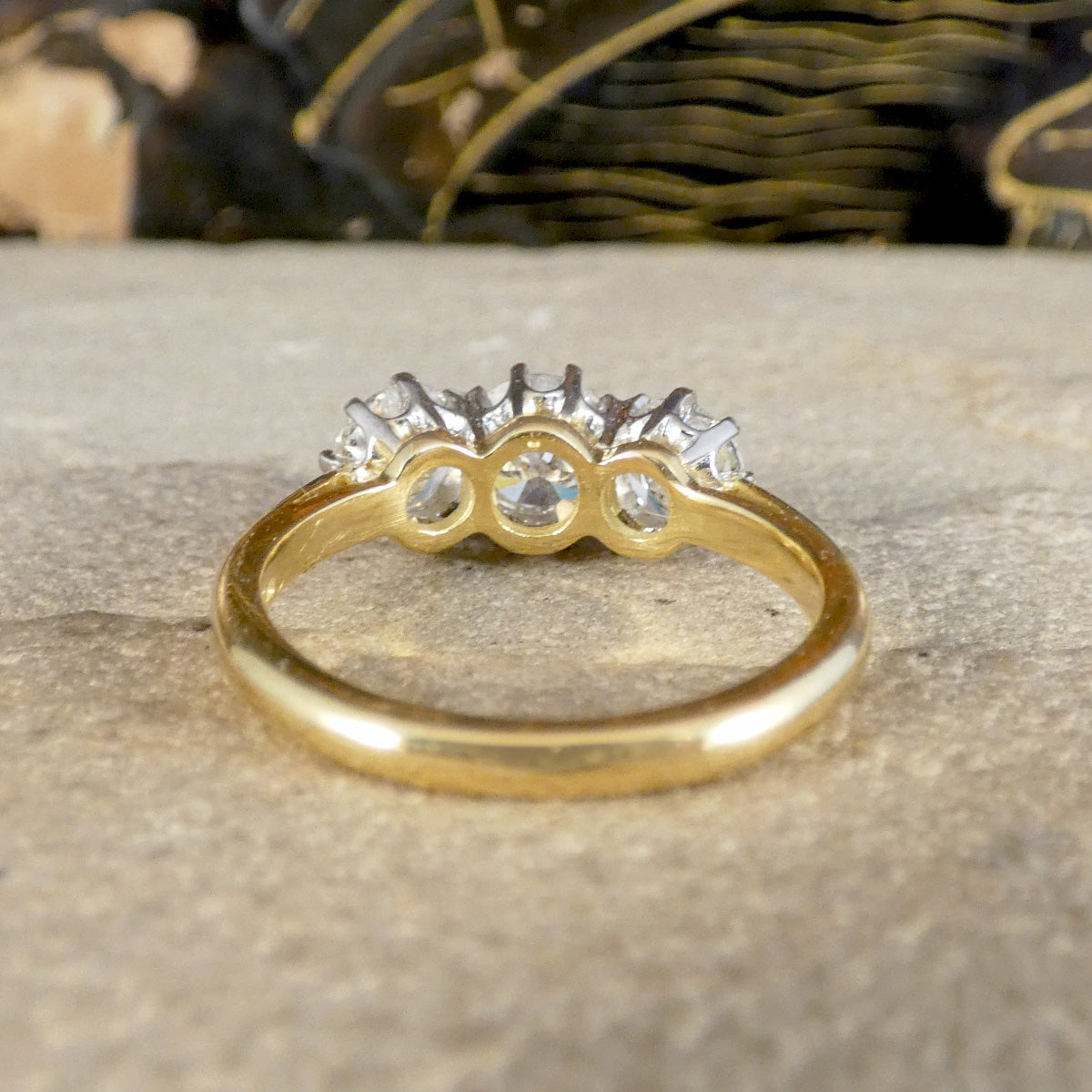 A yellow gold ring with a three-stone cluster setting featuring clear gemstones, resting on a textured stone surface.