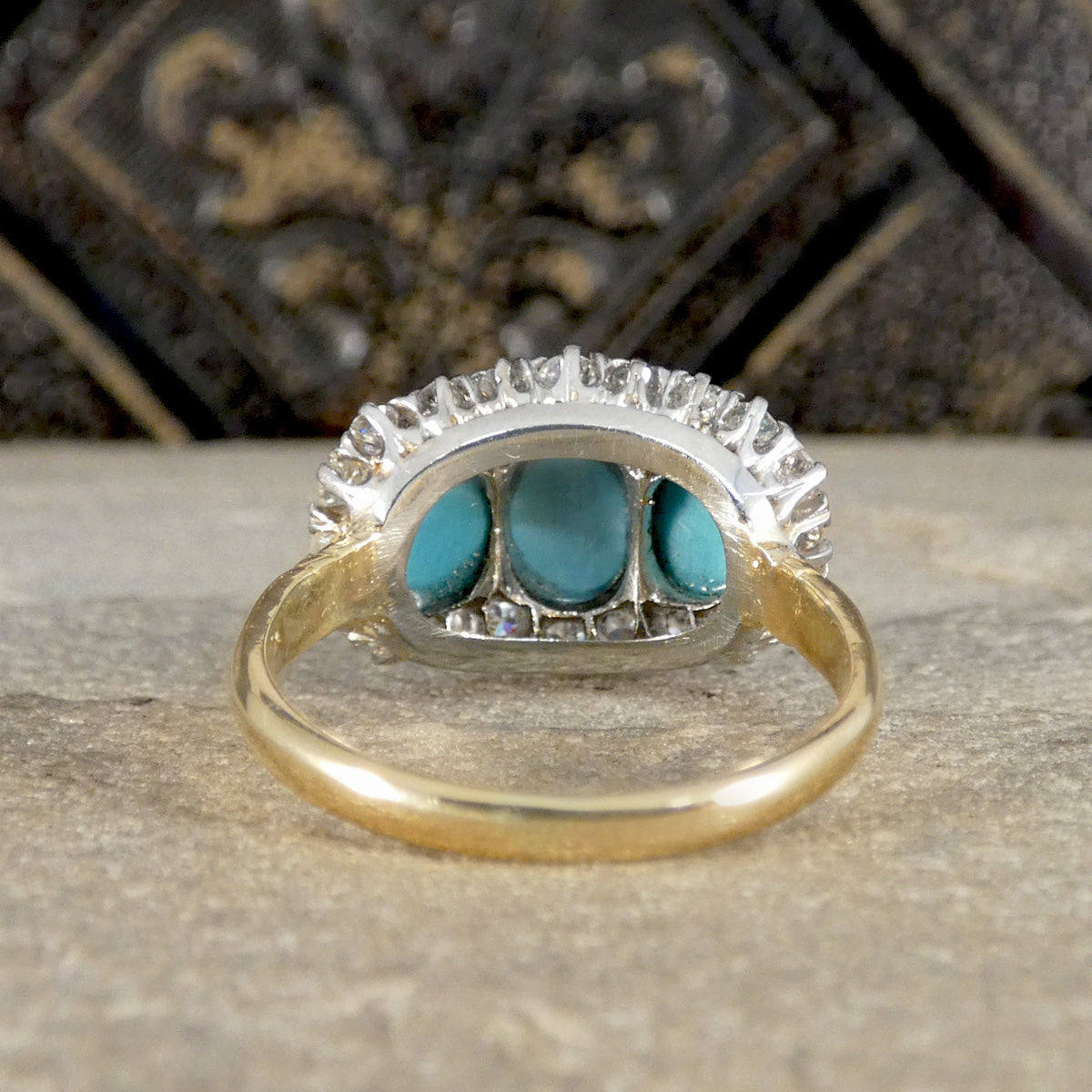 Gold and silver ring with turquoise stones on a textured surface