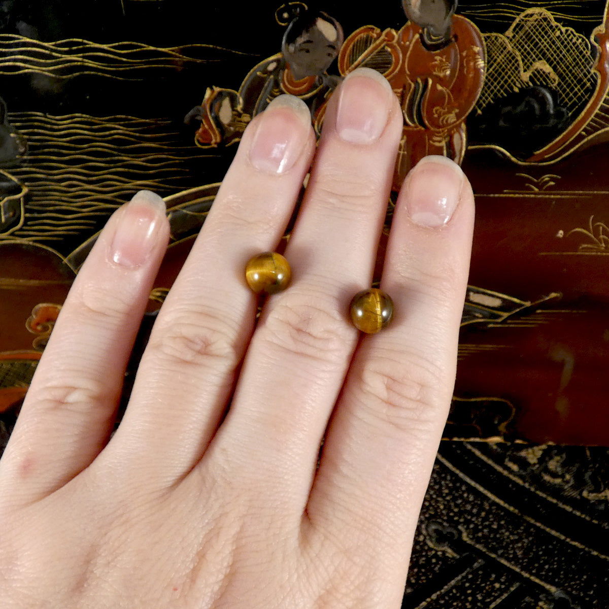 a pair of tigers eye stud earrings displayed on a hand.
