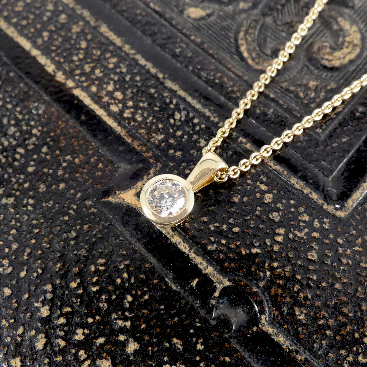 Gold necklace with a diamond pendant on a textured black surface