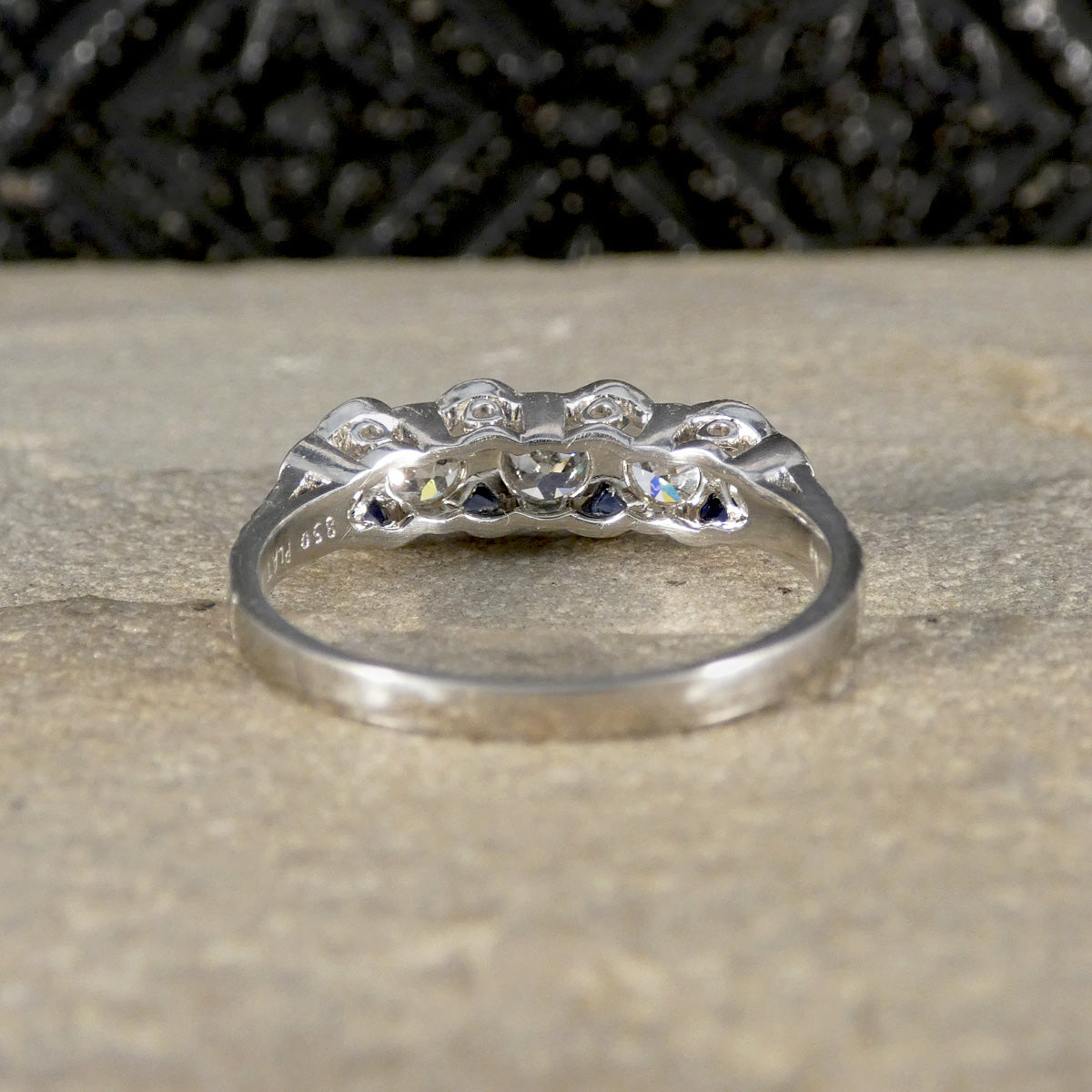 Rear view of an intricately crafted platinum ring showcasing openwork detailing behind old-cut diamonds and blue sapphire accents, highlighting the expert setting and vintage-inspired design.