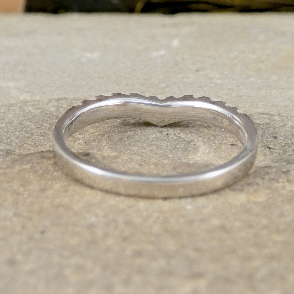 A polished silver band ring with a wavy, scalloped edge, resting on a textured beige stone surface.
