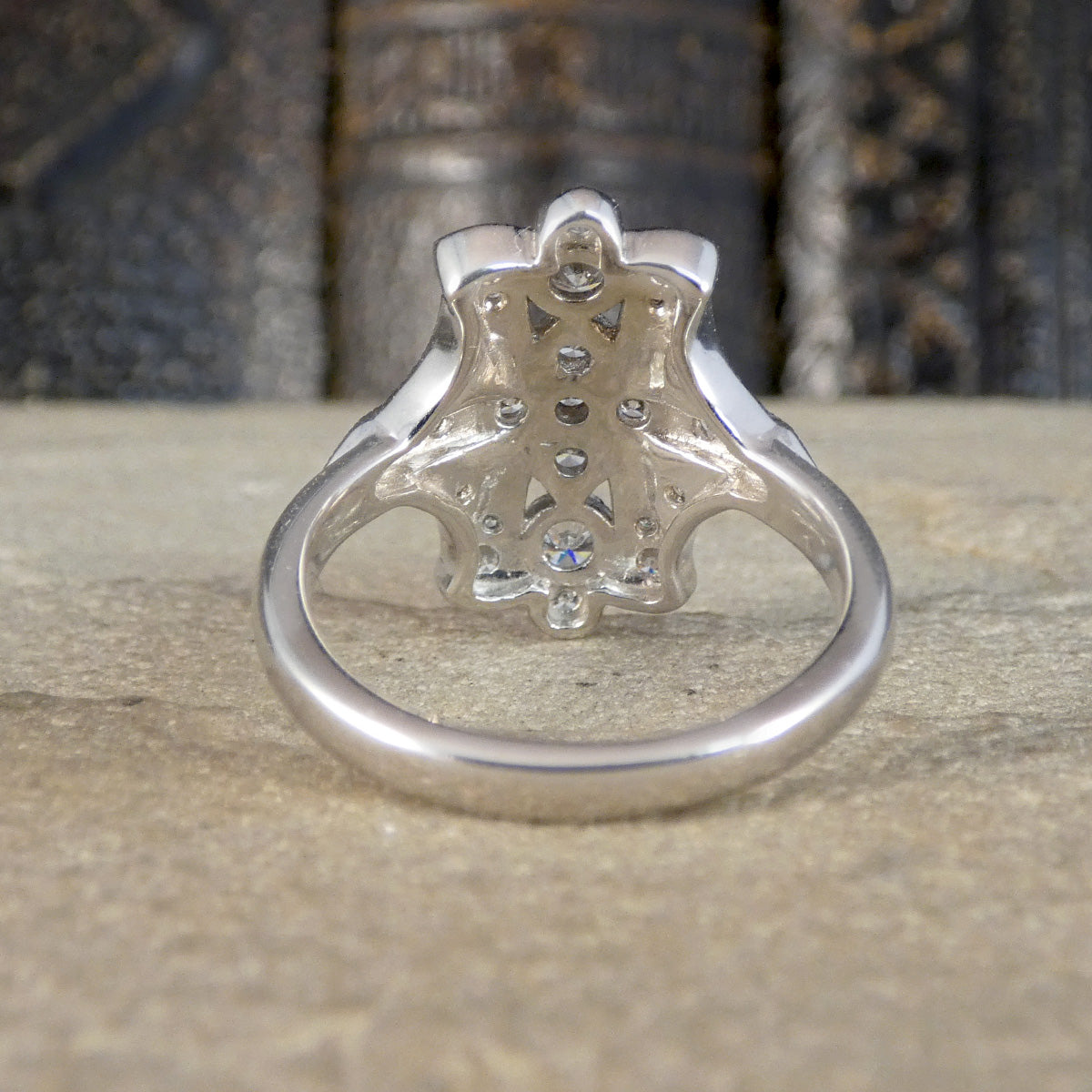 A silver ring with a decorative openwork floral or starburst back setting and small clear stones, photographed on a stone surface with a blurred dark background.