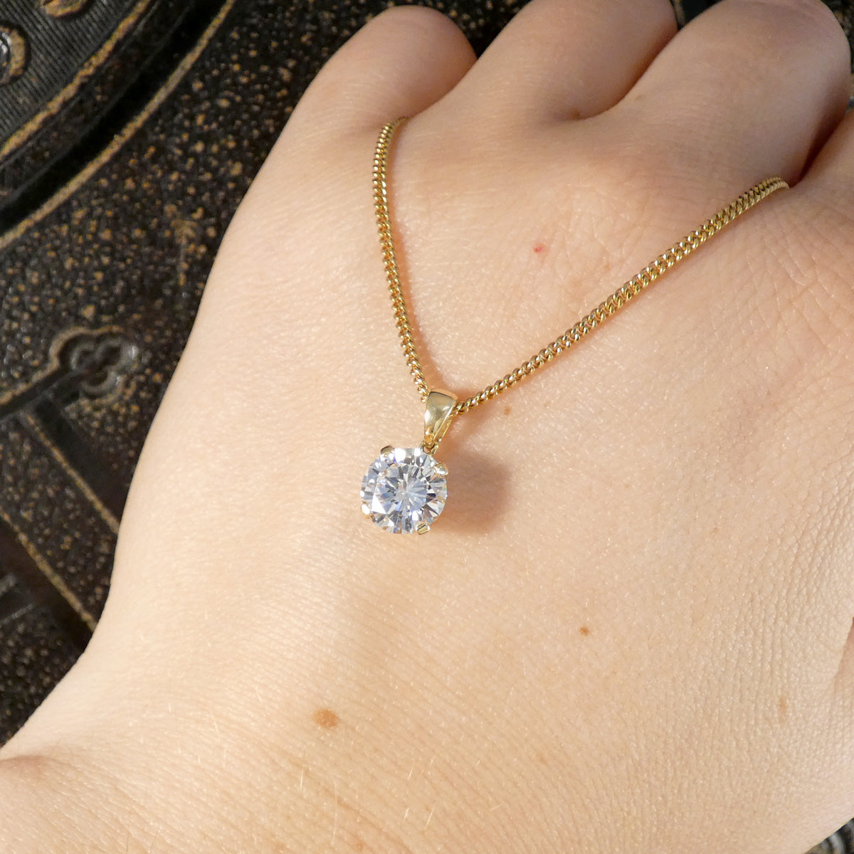 A close-up of a person's hand wearing a delicate gold chain necklace with a round clear gemstone pendant.