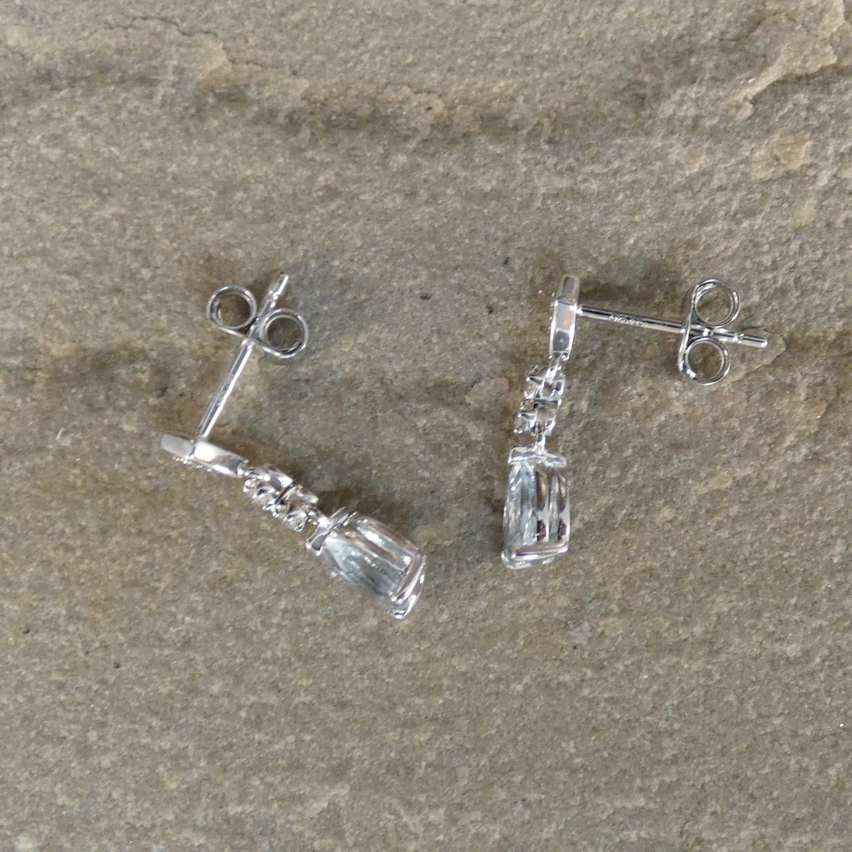 Silver earrings with clear gemstones on a stone surface