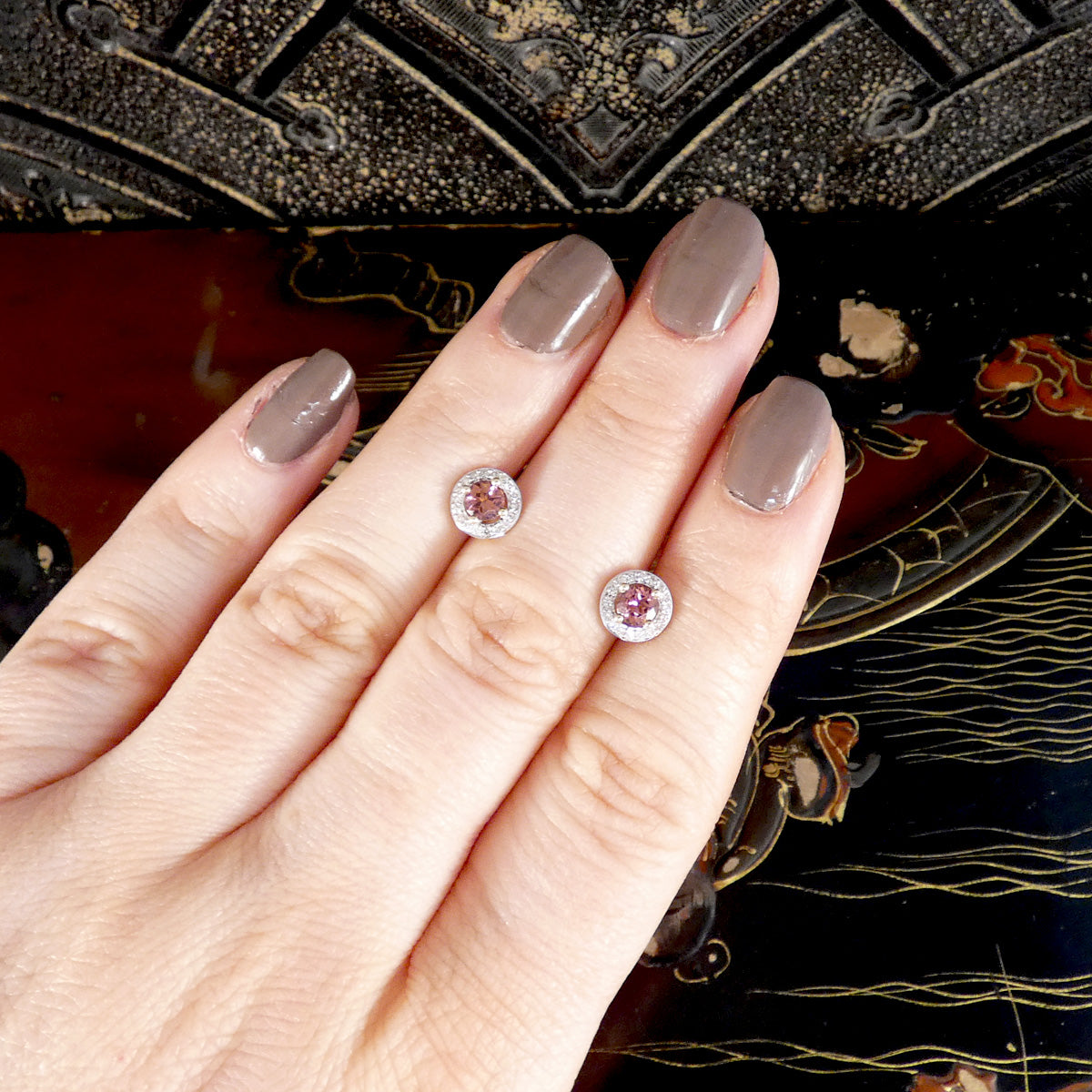 Hand showing two pink gemstone earrings with a decorative background