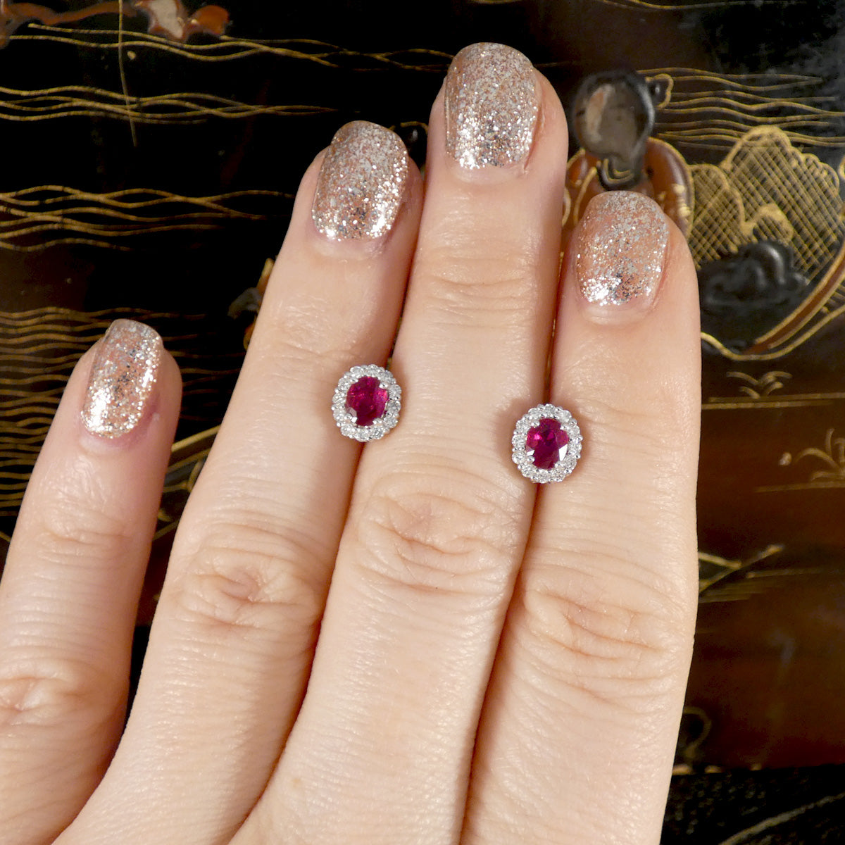Close-up of a hand wearing two ruby and diamond earrings with glittery nail polish.