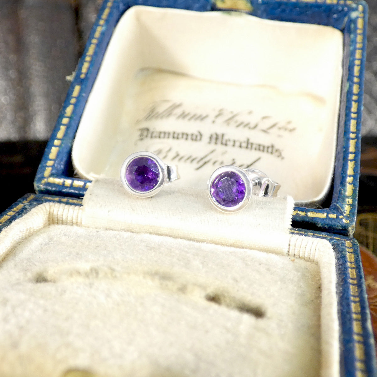 Pair of amethyst gemstone stud earrings in an open jewellery box with visible branding.