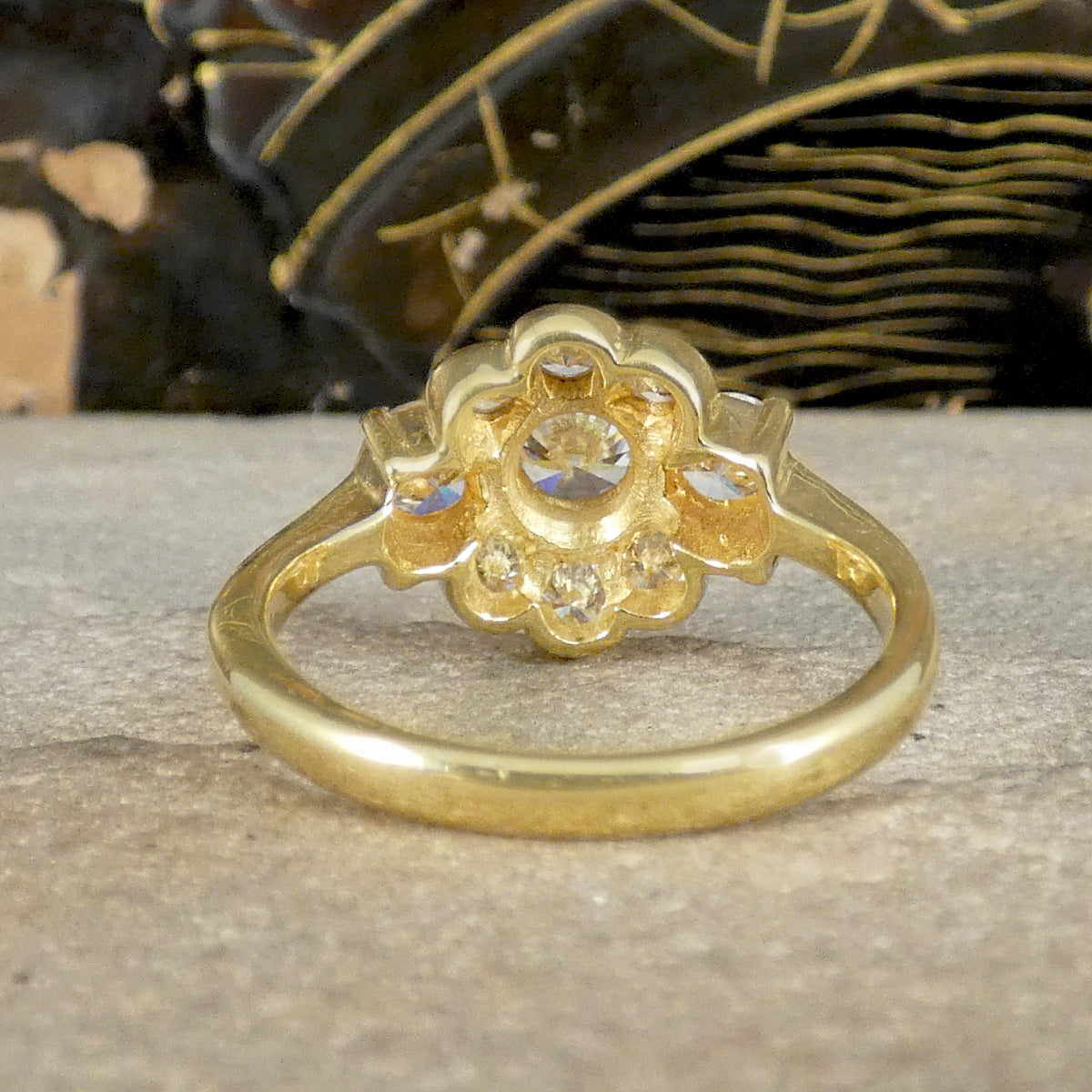 Gold ring with floral design and embedded stones on a textured surface.