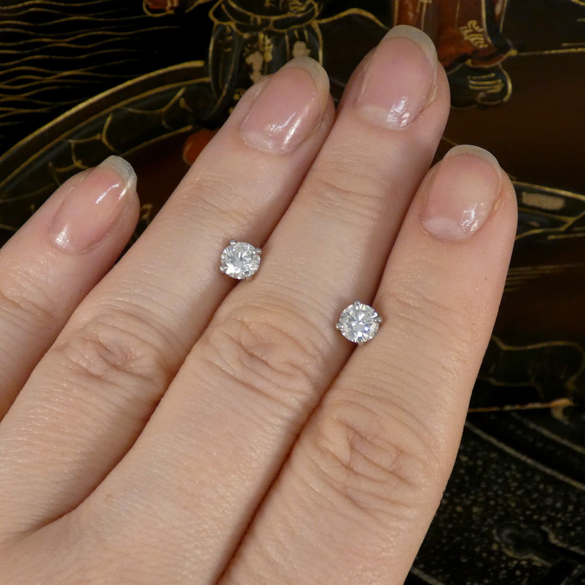A pair of diamond stud earrings displayed on a hand.