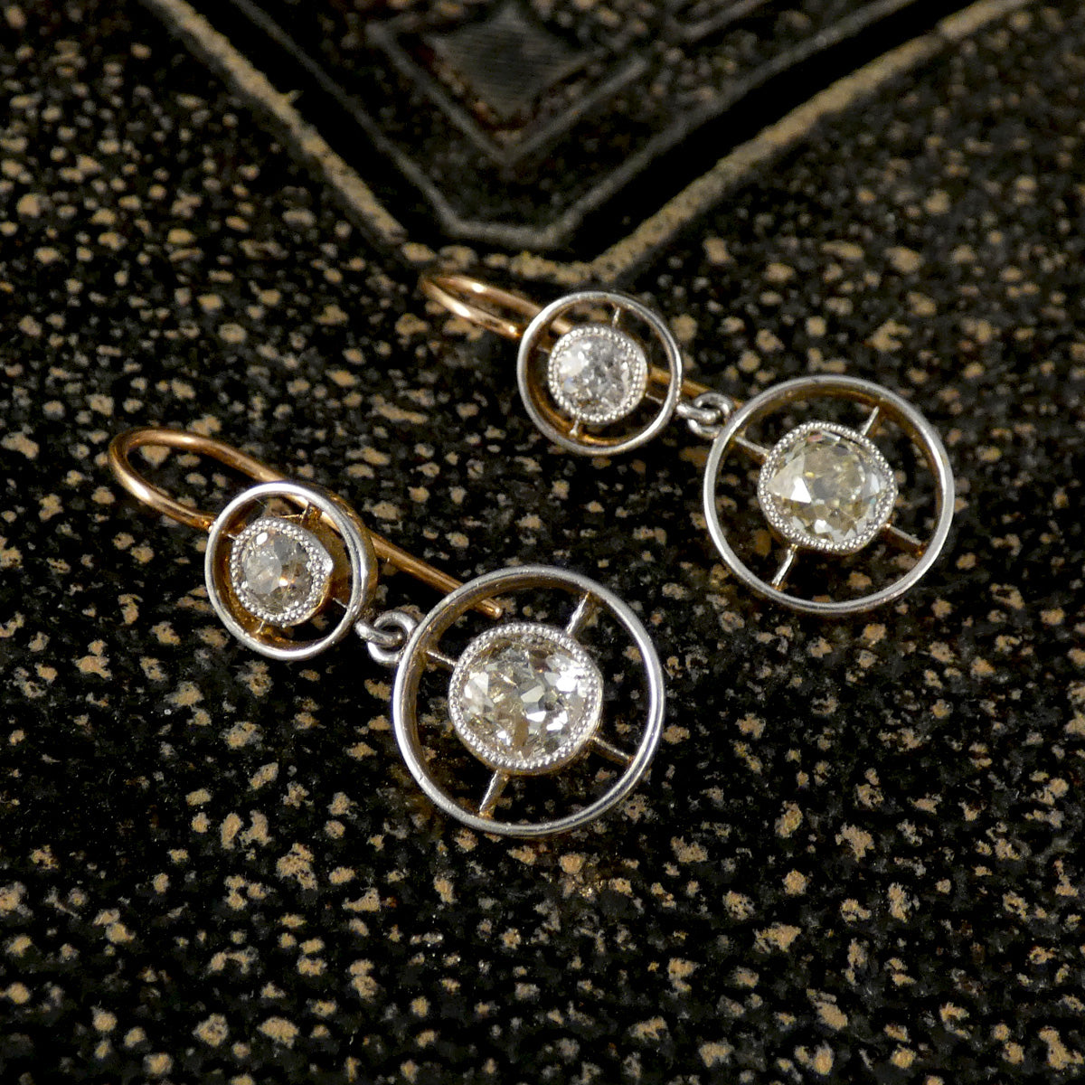 Pair of diamond earrings on a textured black surface