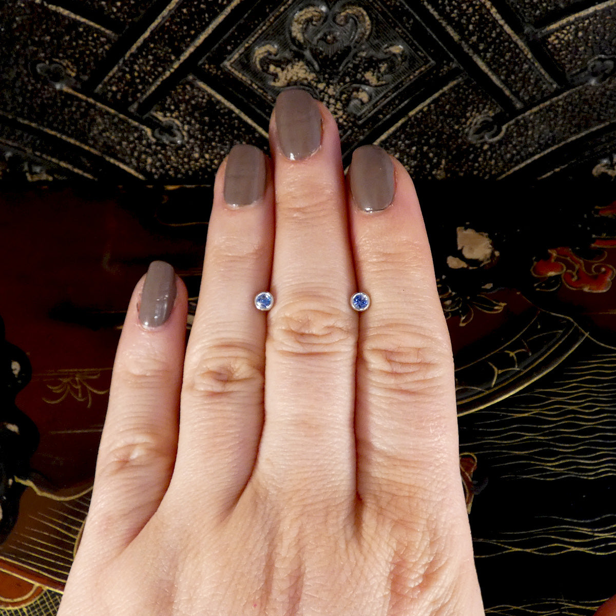A pair of blue sapphire stud earrings in white gold displayed on the hand.