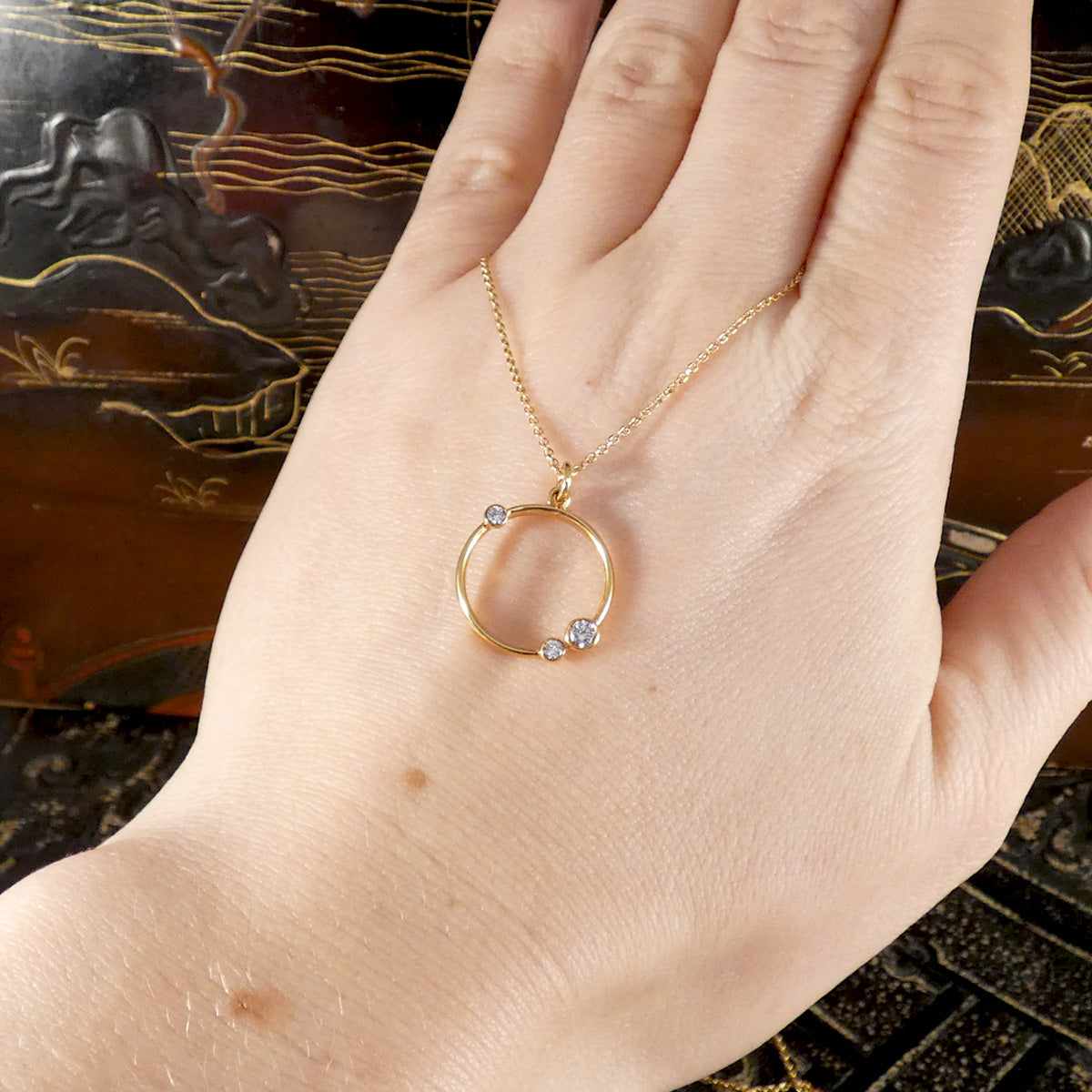 Gold necklace with a circular pendant on a hand against a decorative background