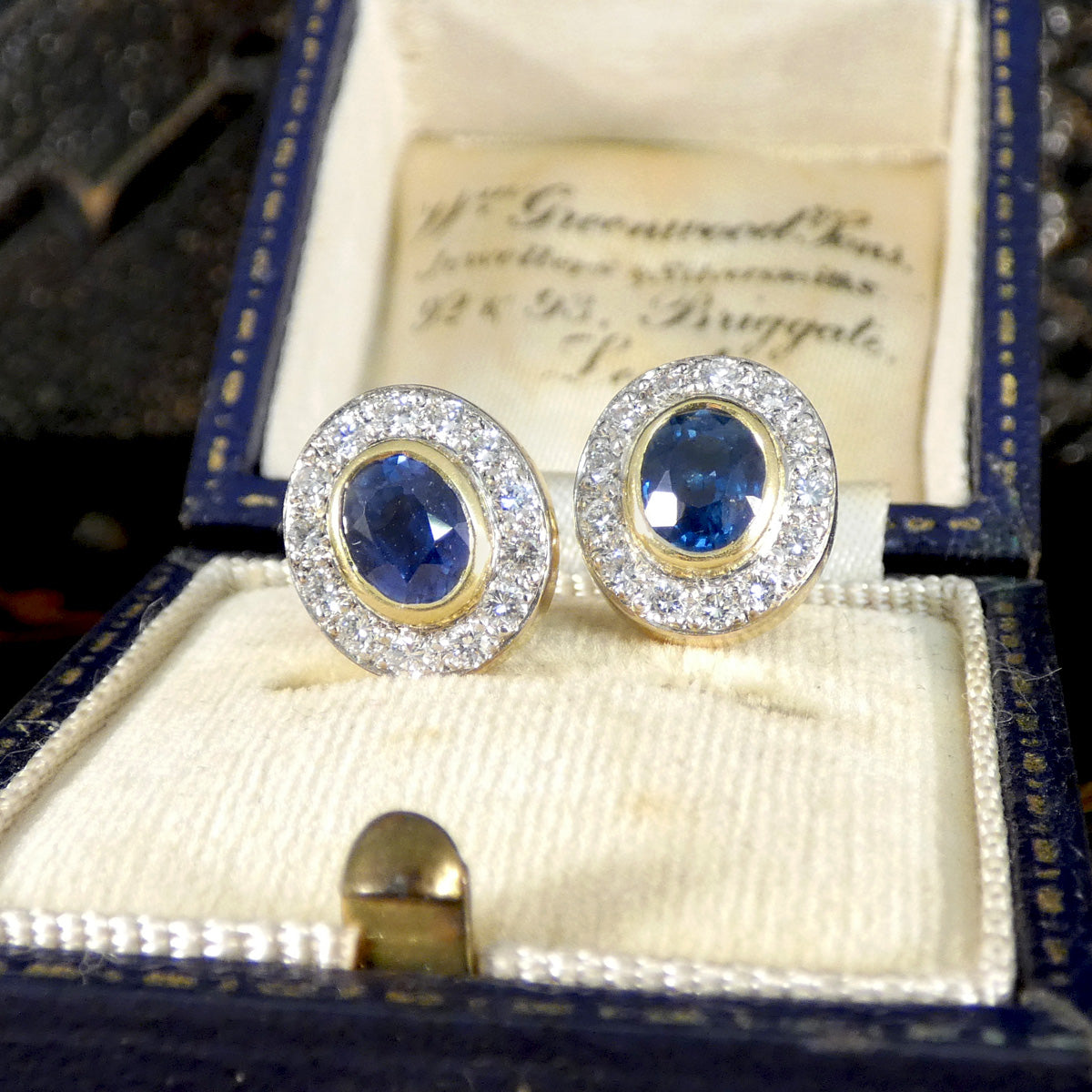 A beautifully bright pair of sapphire and diamond stud earrings in 18ct gold with a bezel setting.