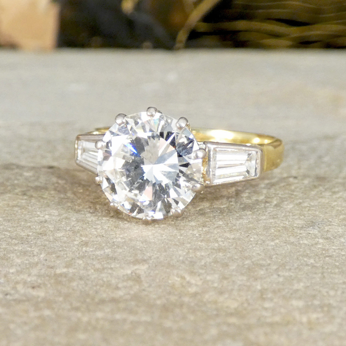 Gold ring with a large diamond and smaller baguette-cut diamonds on a textured surface