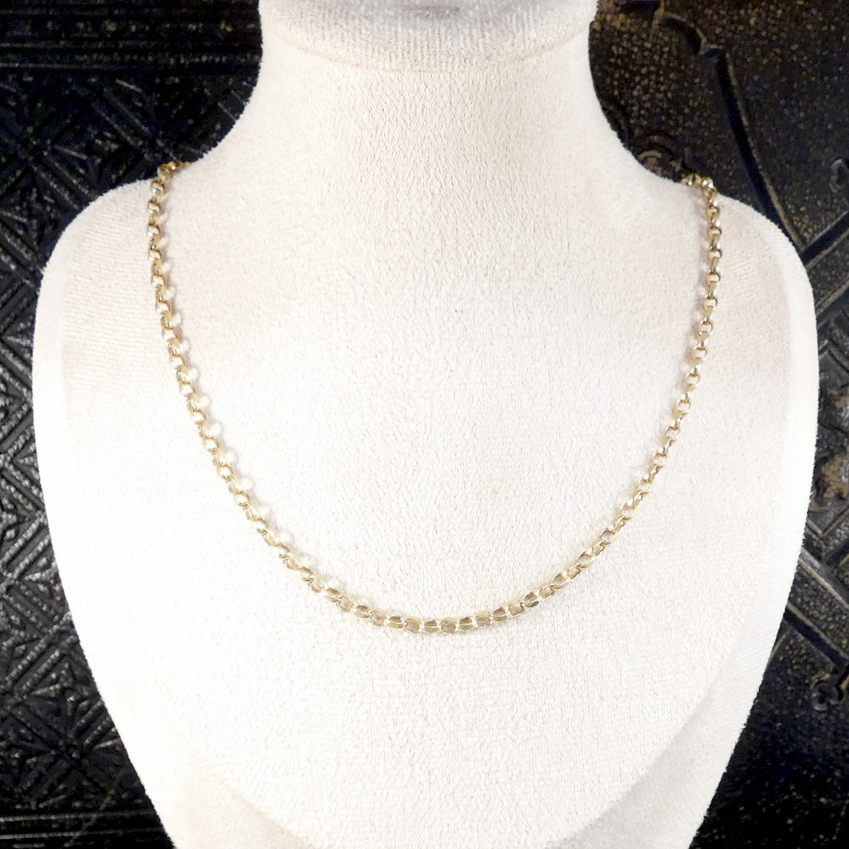 A gold chain necklace displayed on a white fabric-covered mannequin bust against a dark textured background.
