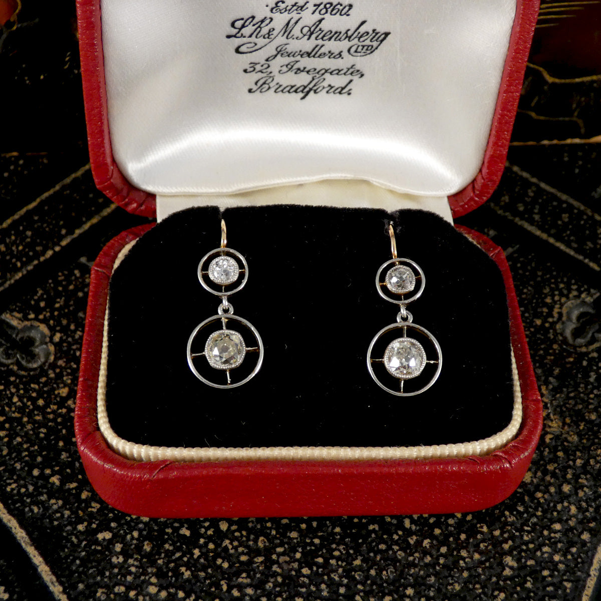 Pair of diamond set earrings with circular design in a red jewelry box.
