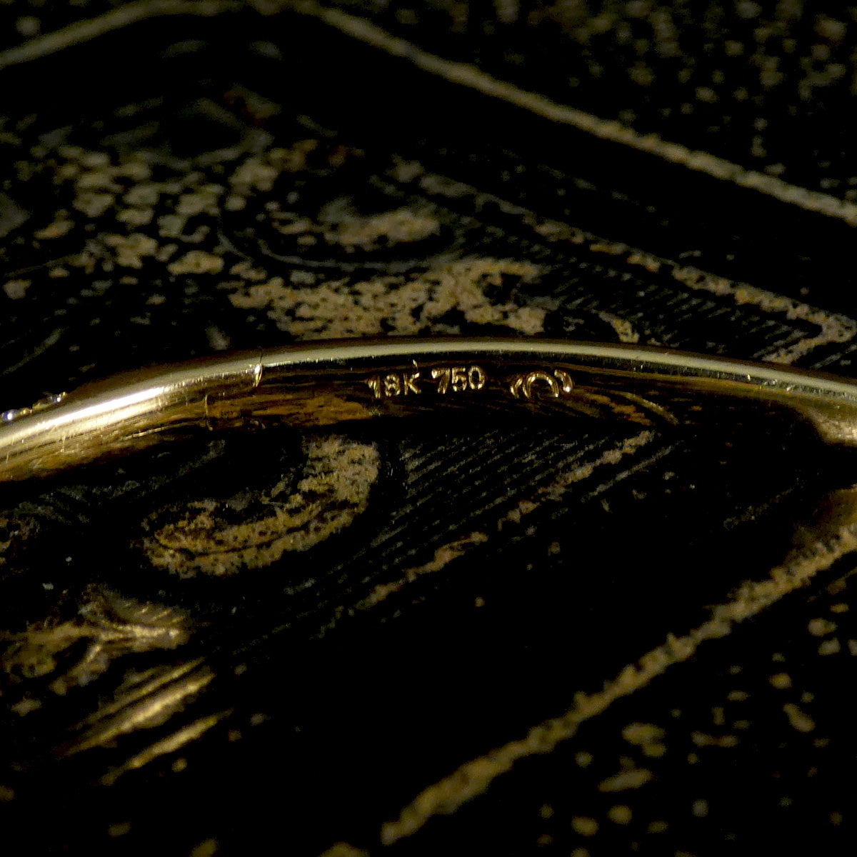Close-up of a gold bracelet with '18K 750' marking on a dark background