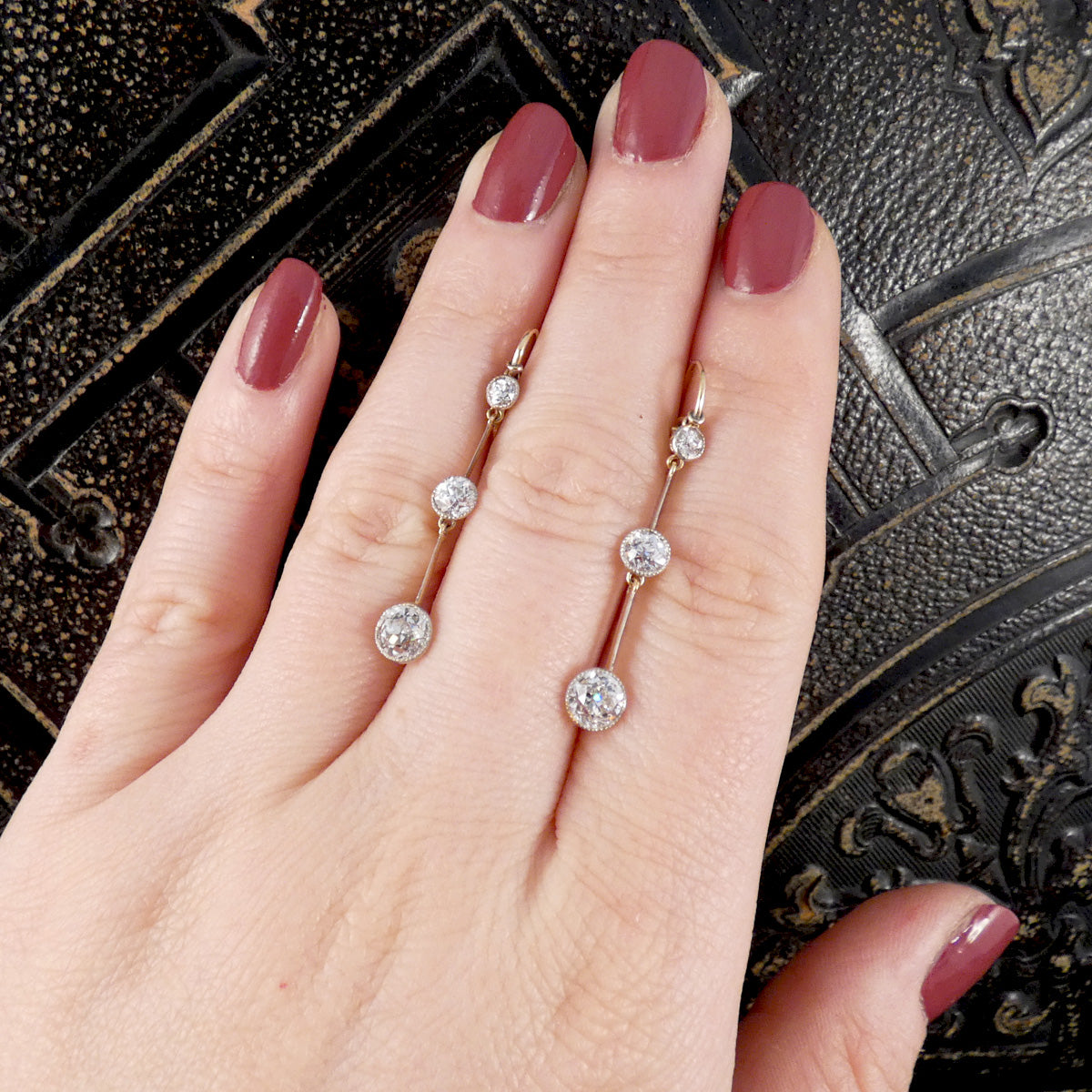 Hand showing a pair of diamond earrings with a decorative background