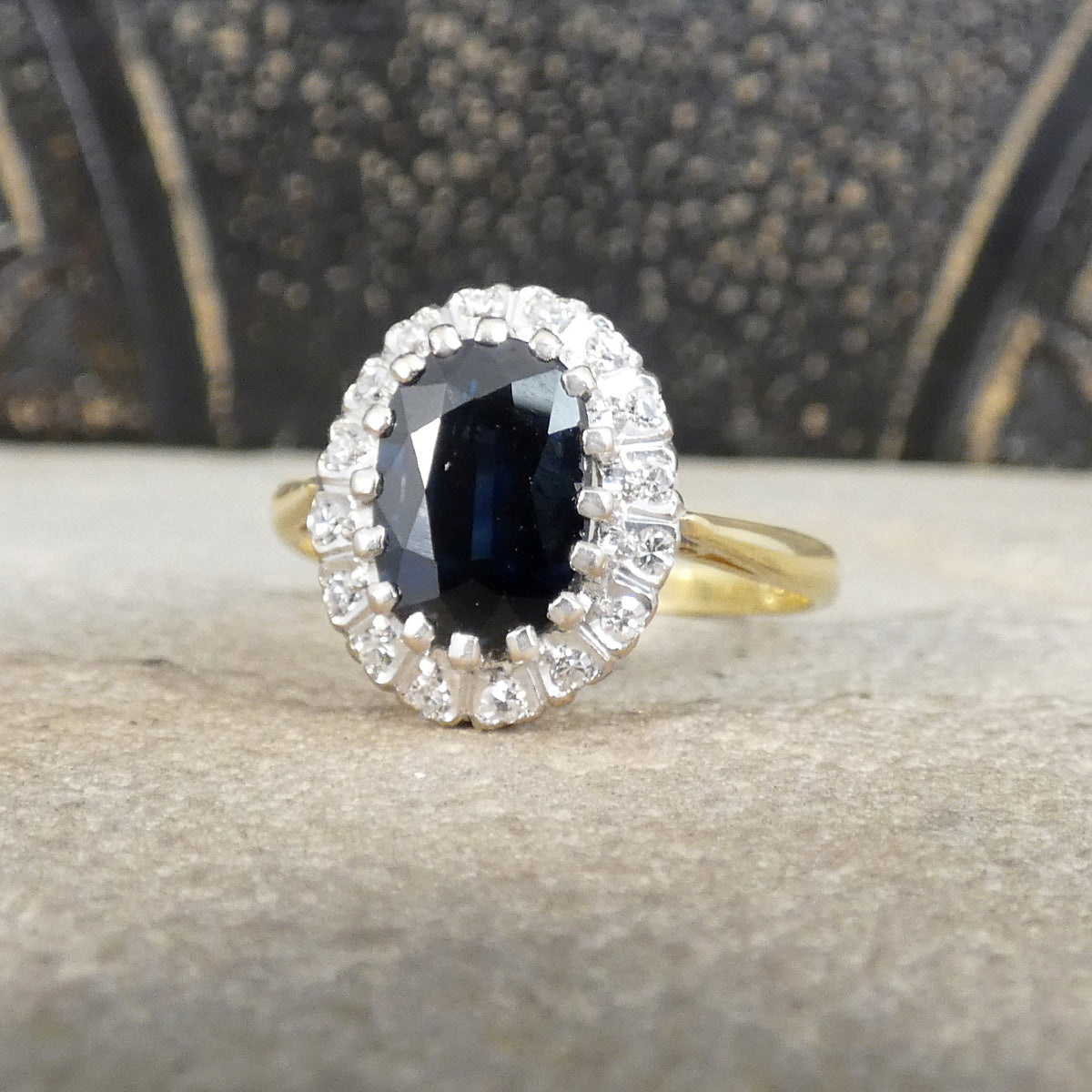 Gold ring with a blue gemstone and diamond accents on a textured surface