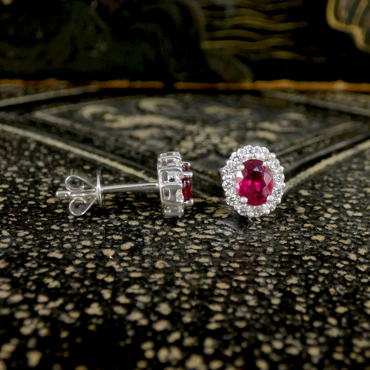 White gold earrings with red ruby gemstones with diamond cluster on a textured surface
