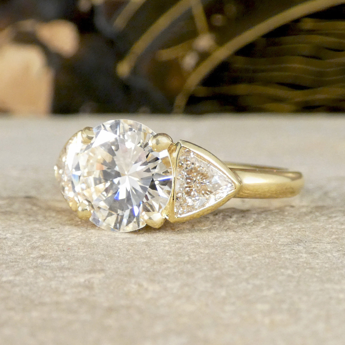Gold engagement ring with a large diamond and a smaller pear-shaped diamond on a neutral background
