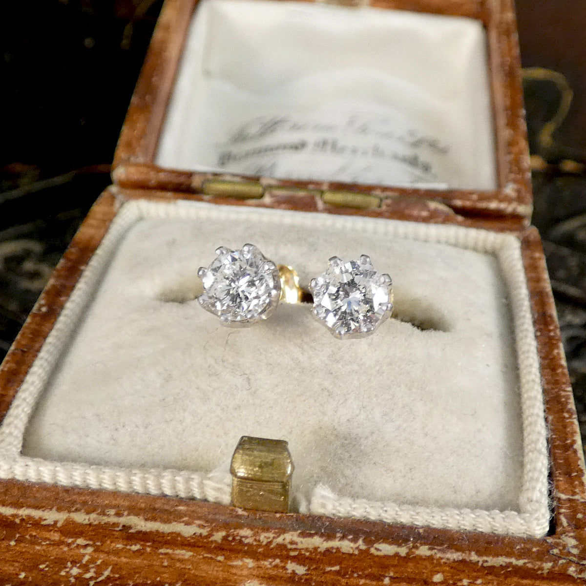 Diamond stud earrings in an open wooden jewelry box.