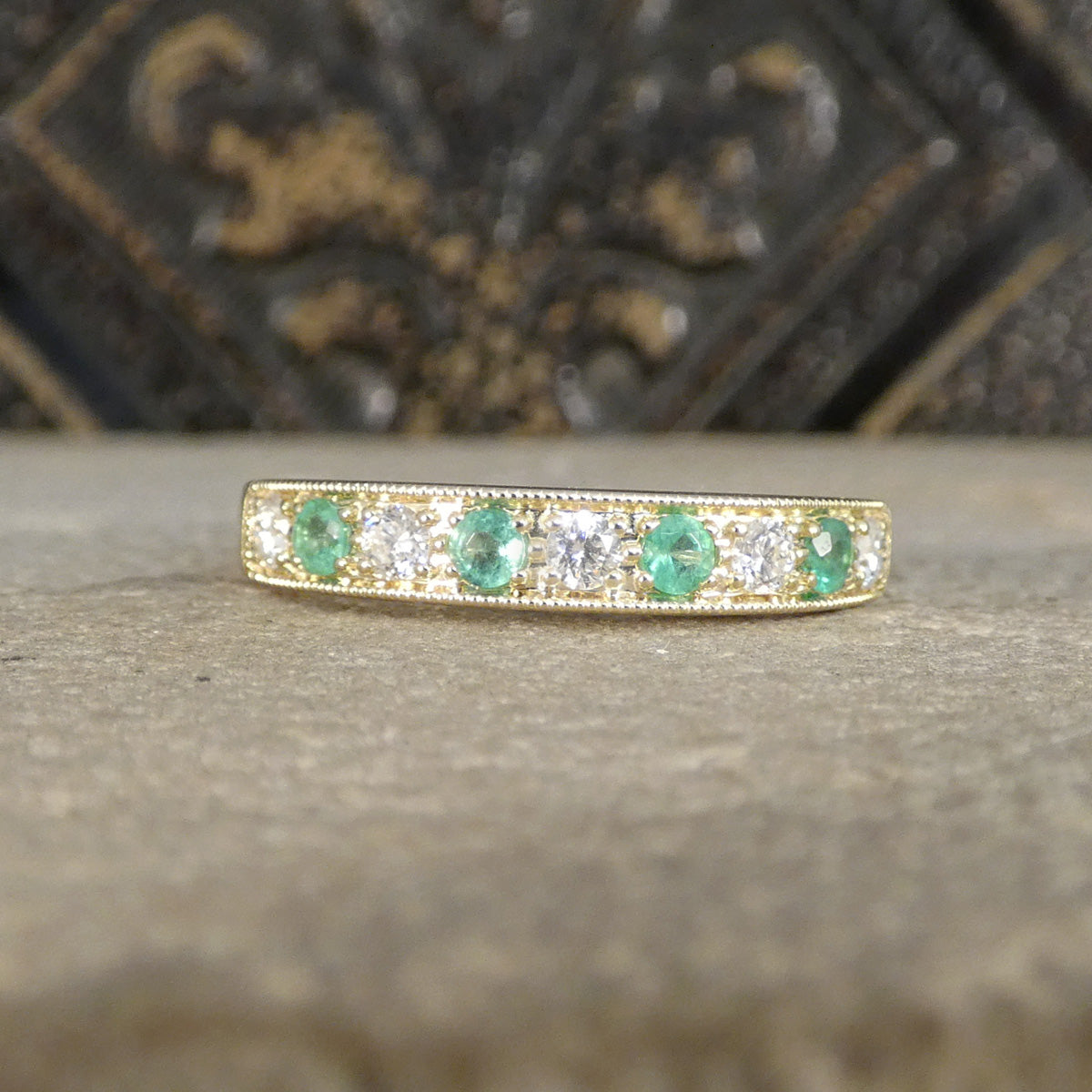 Gold ring with emeralds and diamonds on a textured surface