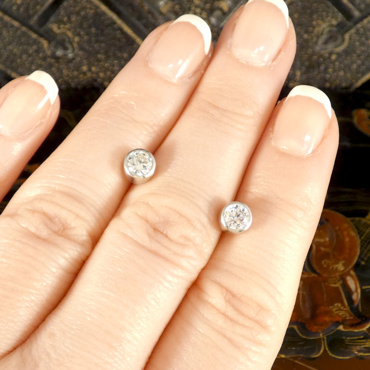 A classic pair of Bezel set Diamond Stud Earrings in Platinum holding 0.80ct with a GIA cert and bright E Colour grading. Displayed on the hand to see size and shape reference. 