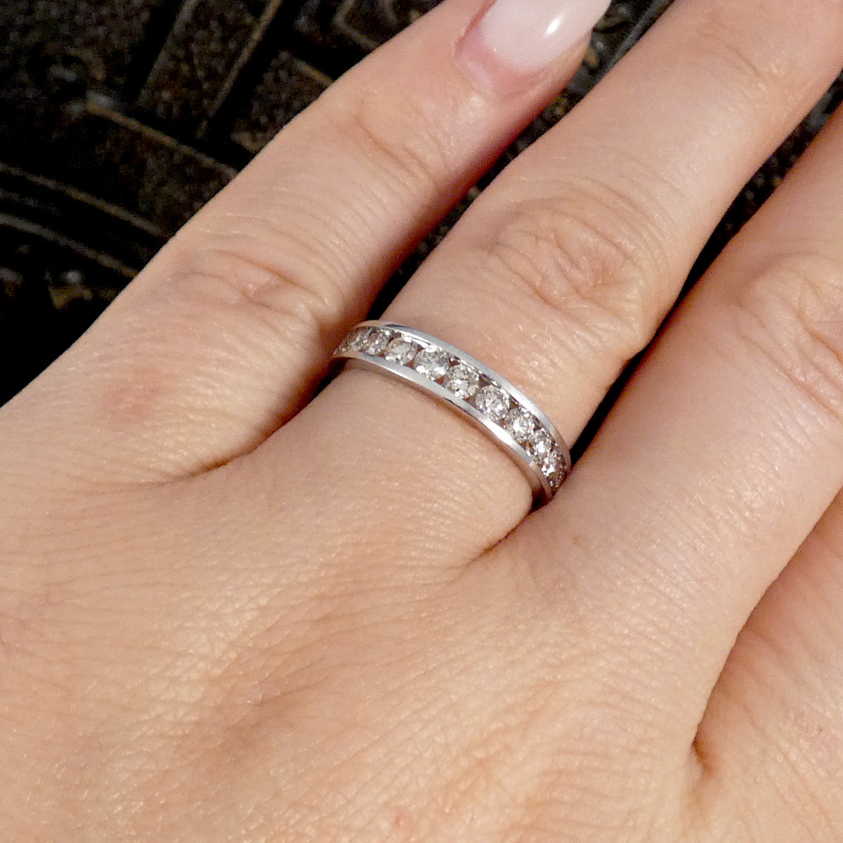 A white gold eternity ring with small clear stones set all around the band, shown worn on a person's ring finger.