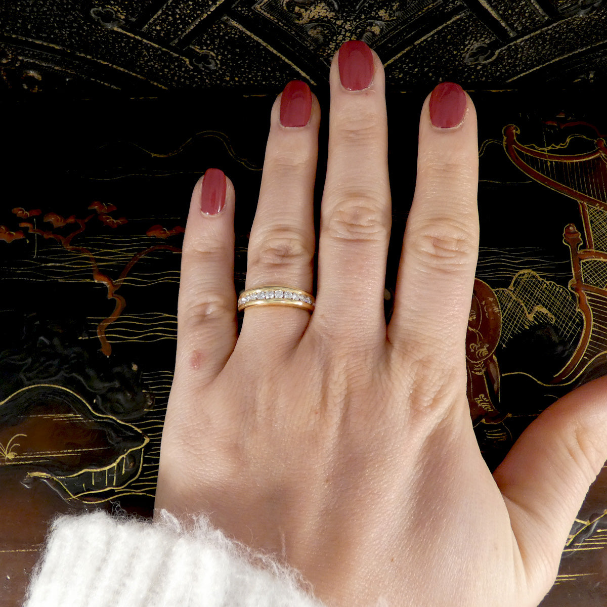 Hand wearing a gold ring with red nail polish against an ornate background
