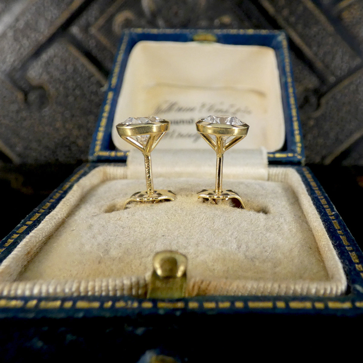 A pair of gold post earrings with clear gemstones, displayed in an open vintage blue jewelry box with a cream velvet insert.