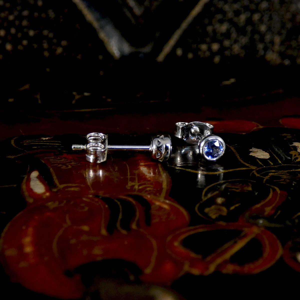 Silver earrings with blue gemstones on a dark, ornate surface