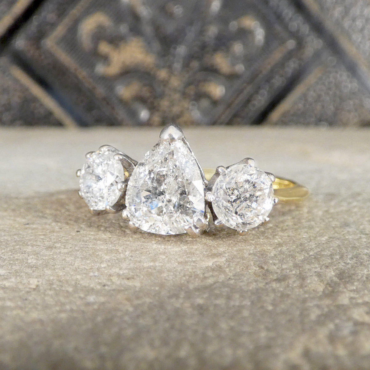 Diamond ring with three pear-shaped stones on a textured surface