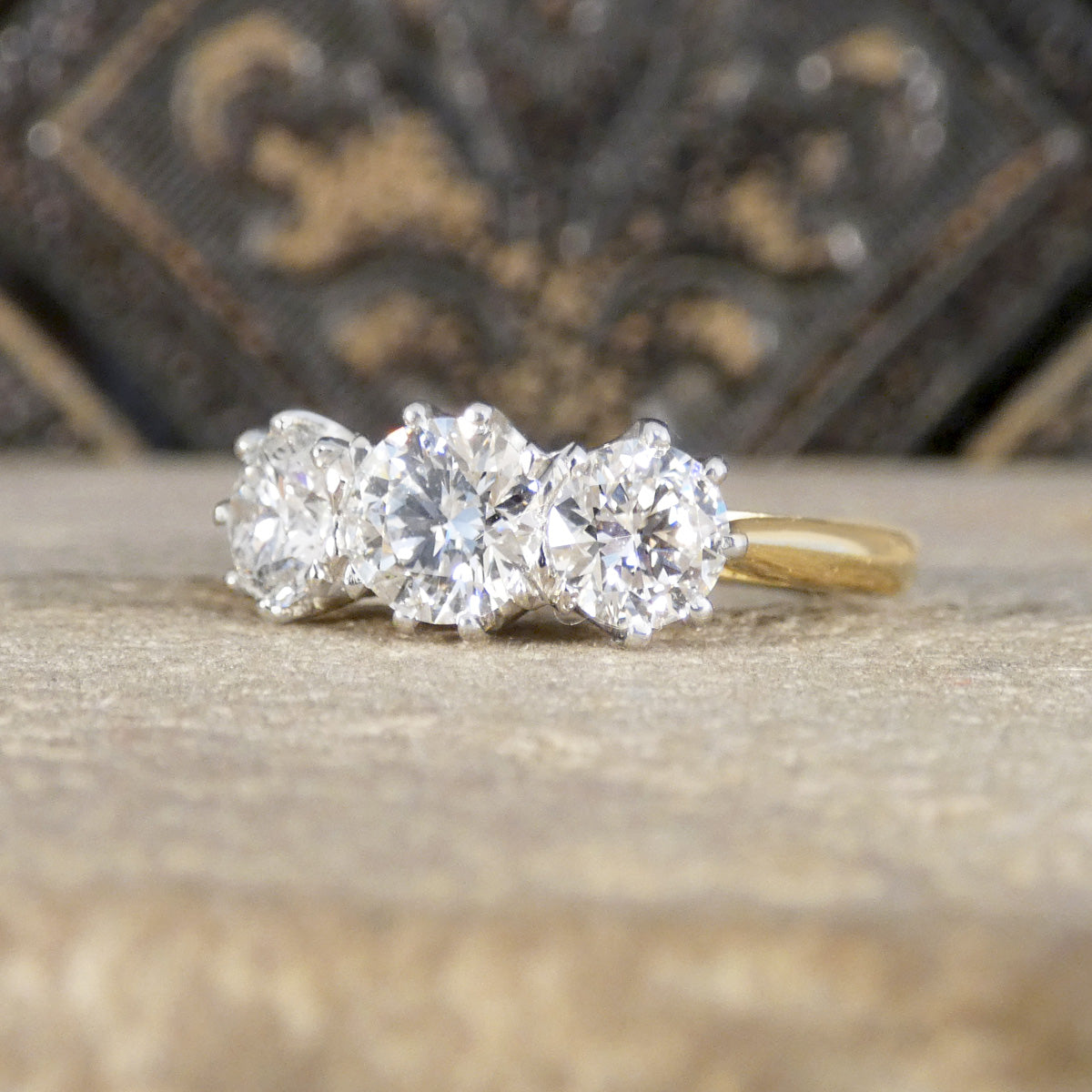 Three-stone diamond ring on a textured surface with a blurred decorative background
