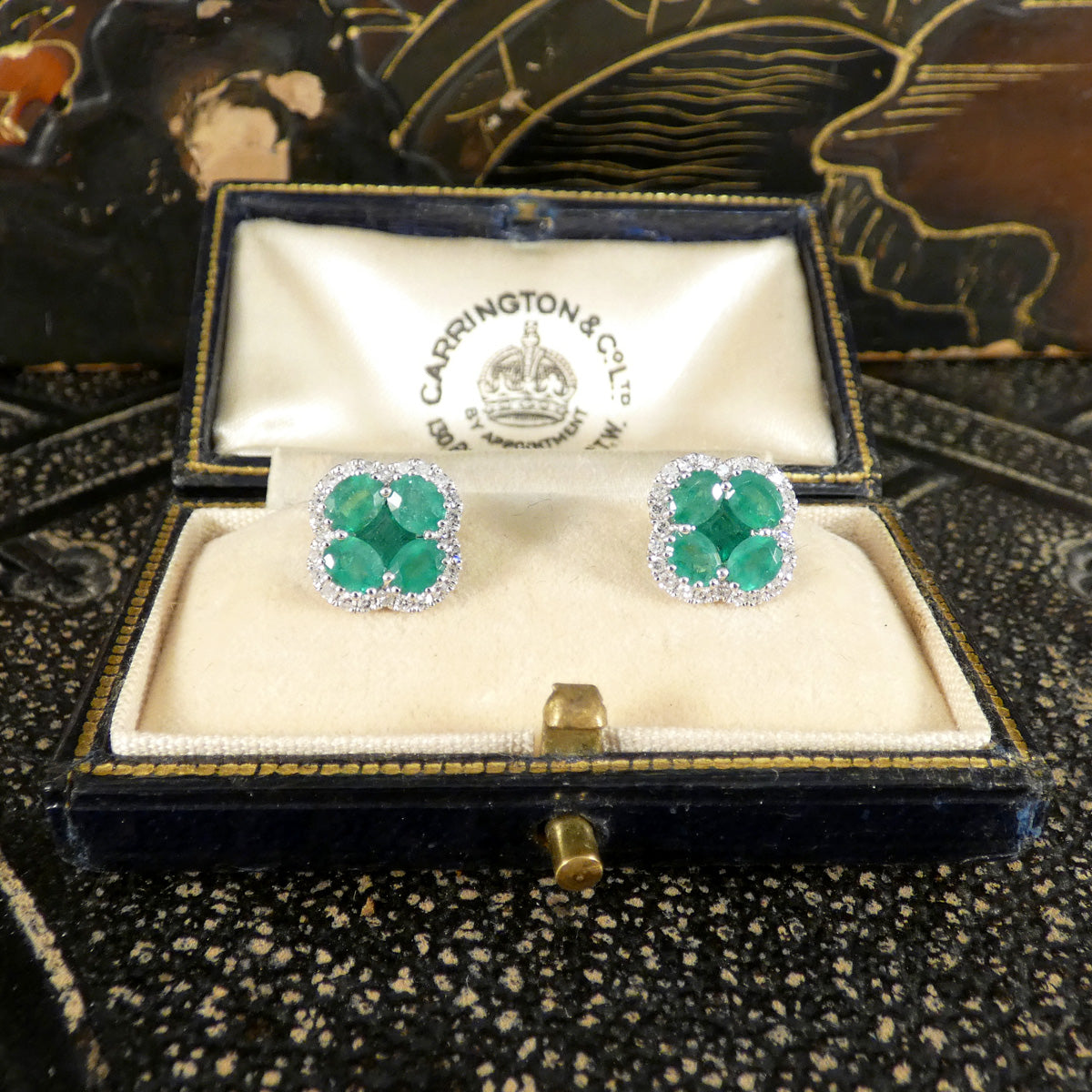 Pair of emerald earrings in a Carrington & Co box on a decorative surface
