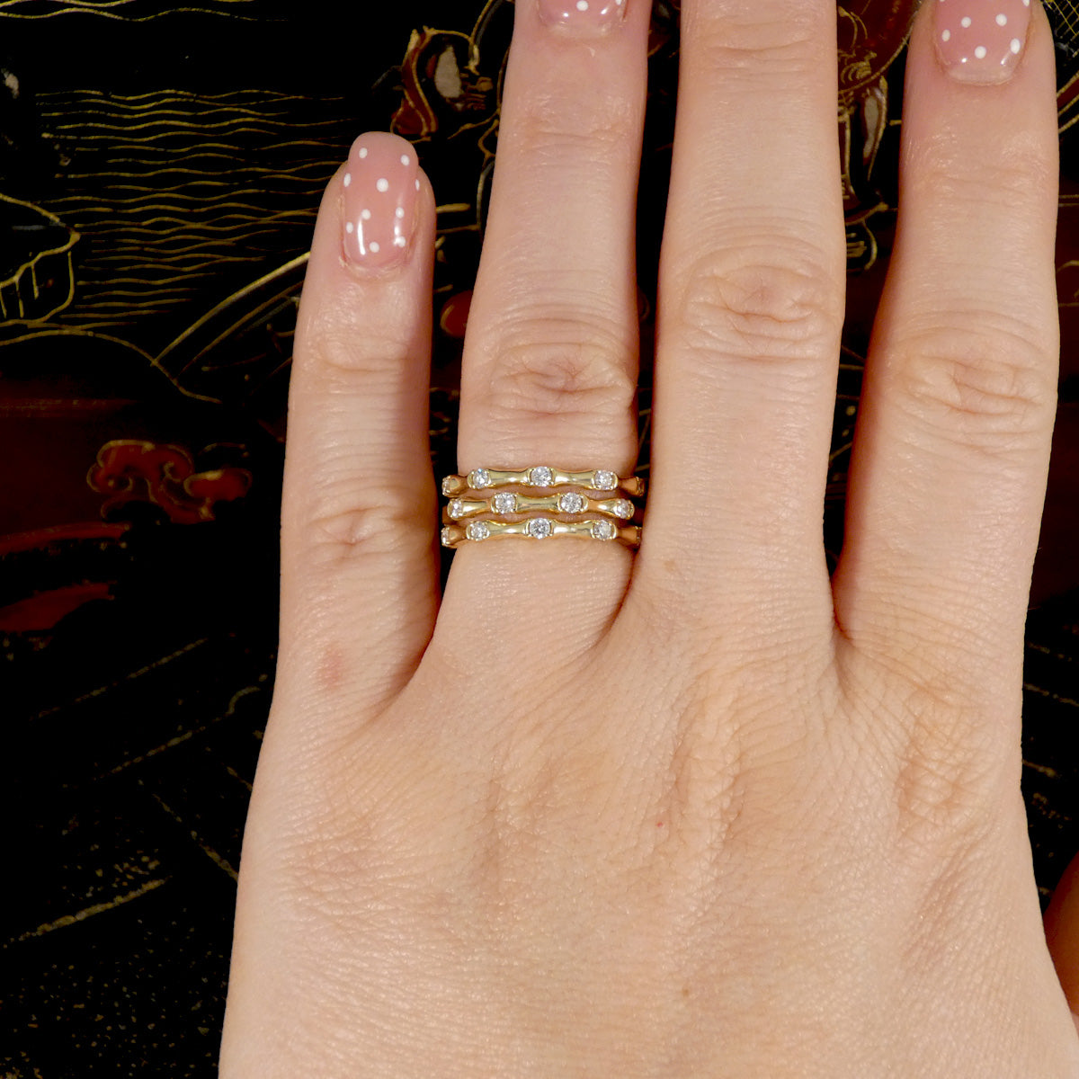 Three strand bamboo style ring in yellow gold with diamonds shown on ring finger on the hand
