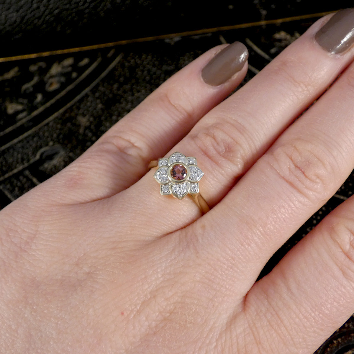 Close-up of a hand wearing a decorative ring with a pink gemstone on a dark background