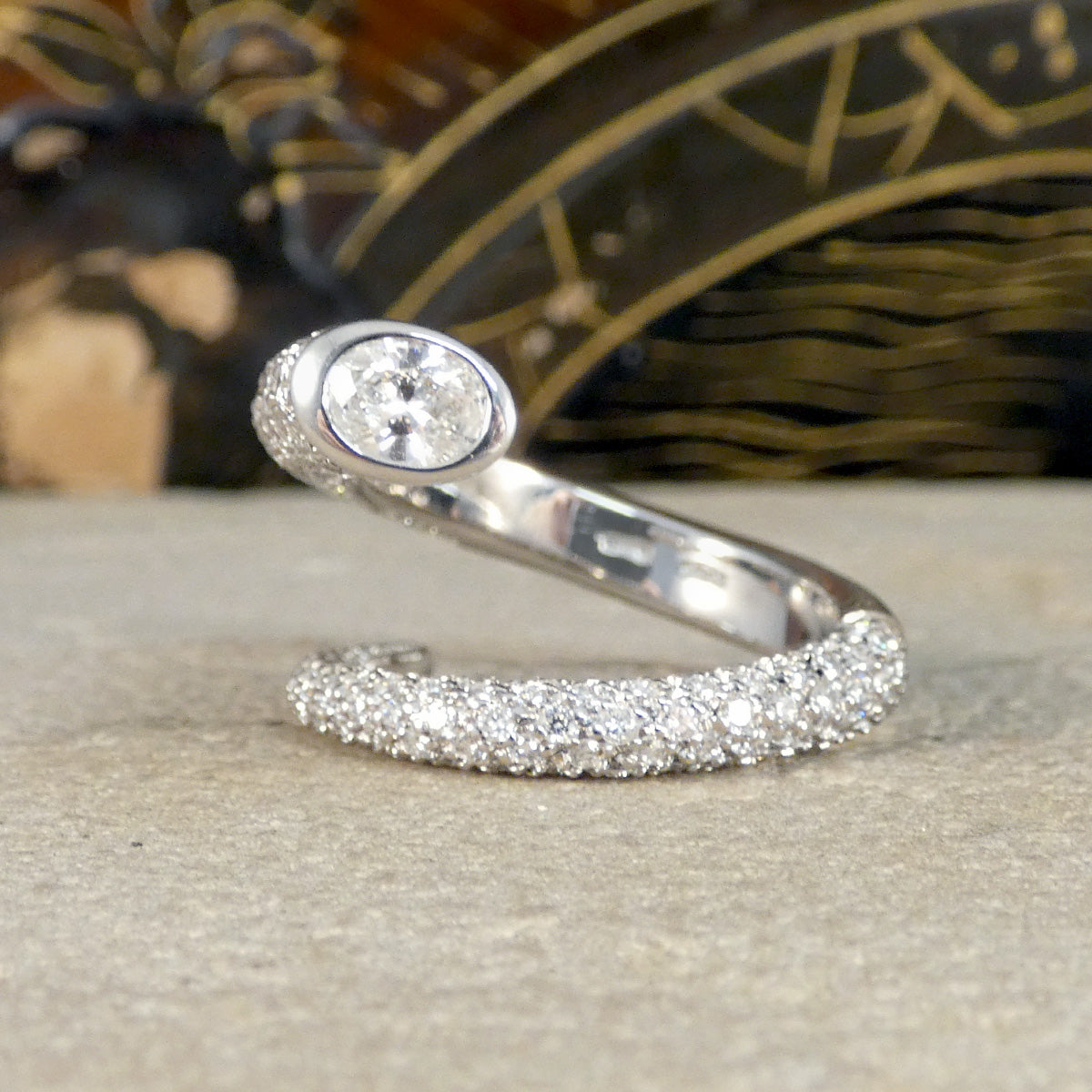 A unique diamond set snake like ring shown on a stone with an oval cut diamond end.