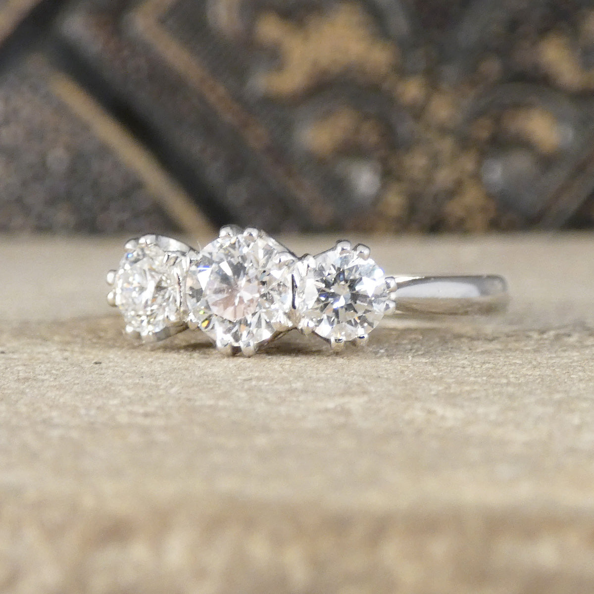 Three-stone diamond ring on a textured surface with a blurred decorative background