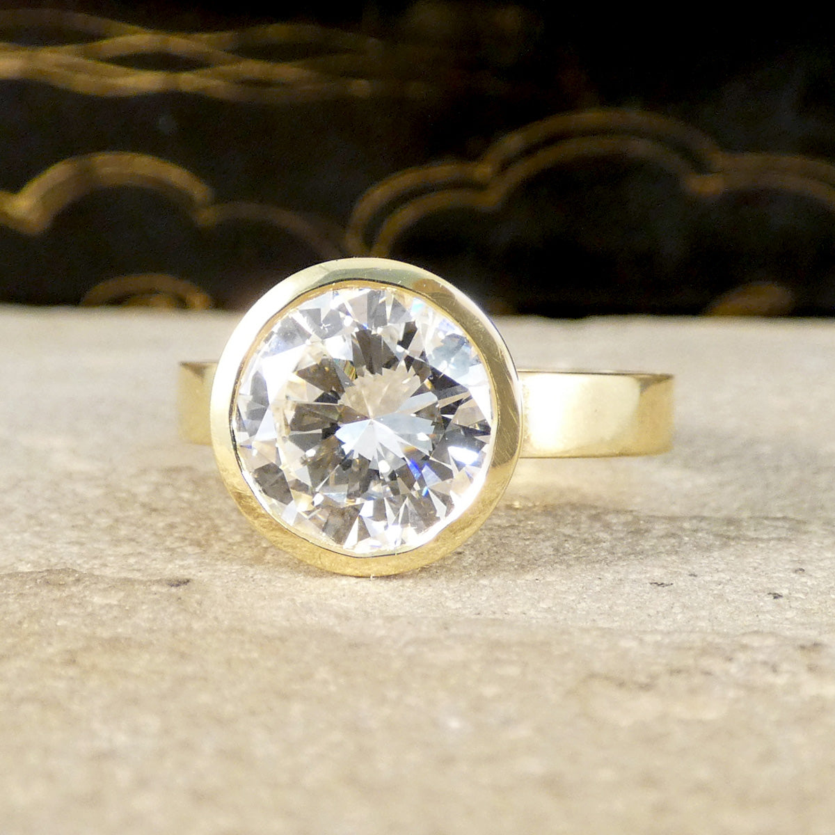 A diamond solitaire ring in a rub over bezel setting in 18ct yellow gold