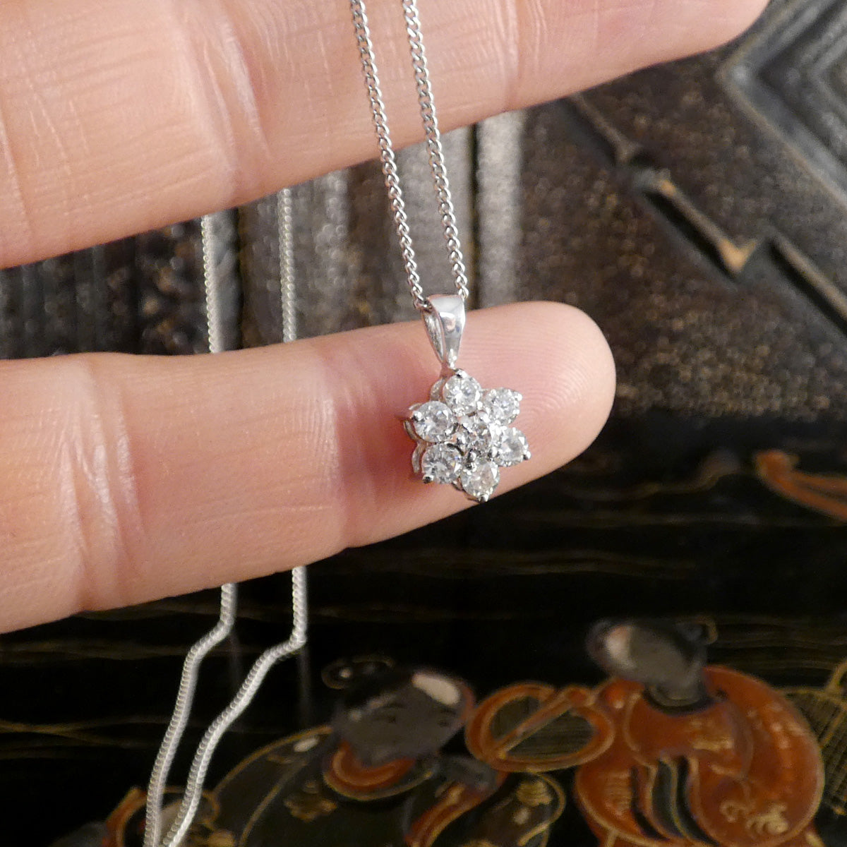 Silver necklace with a floral pendant held between fingers against a textured background