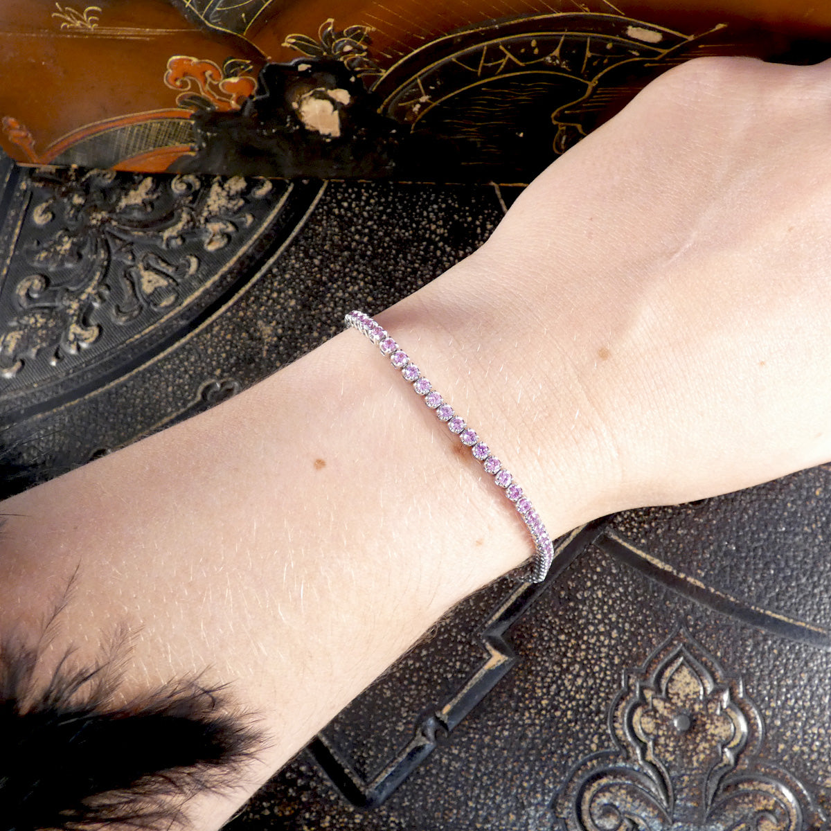 A pink sapphire and diamond tennis bracelet in white gold displayed on a wrist 