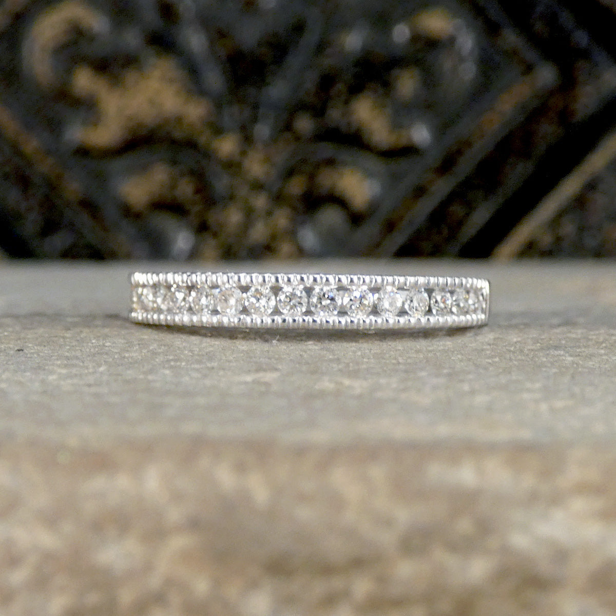 White Gold ring with small stones on a textured surface with blurred background