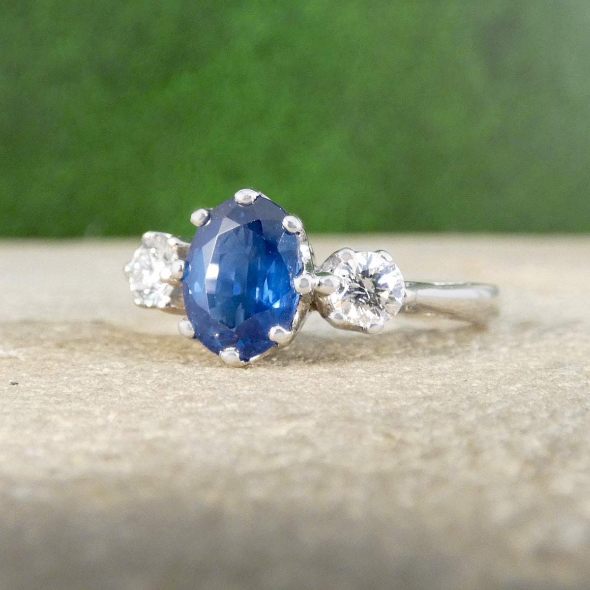 Silver ring with a blue gemstone and smaller diamonds on a textured surface with a green background