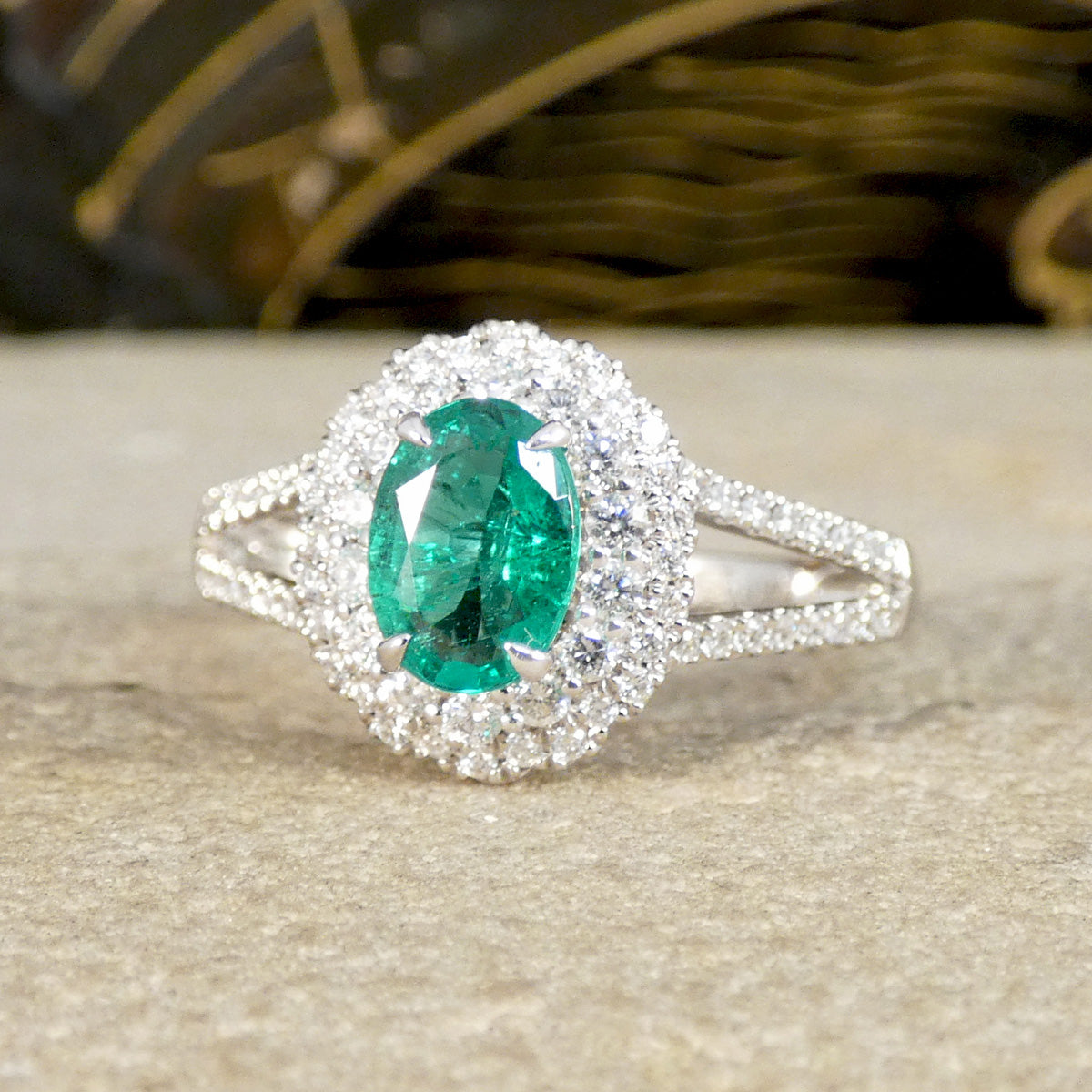 Ring with a green emerald  gemstone and diamond accents on a textured surface