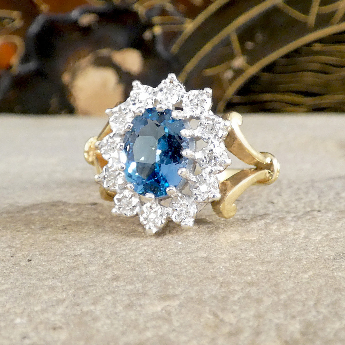 Gold ring with a blue gemstone and diamond accents on a textured surface