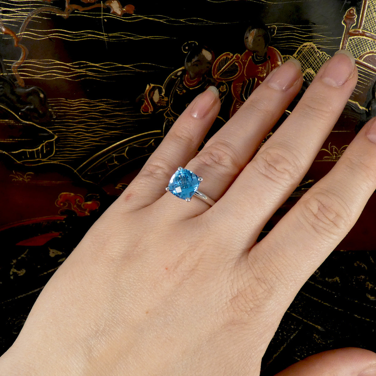 Hand wearing a ring with a blue gemstone against an ornate background