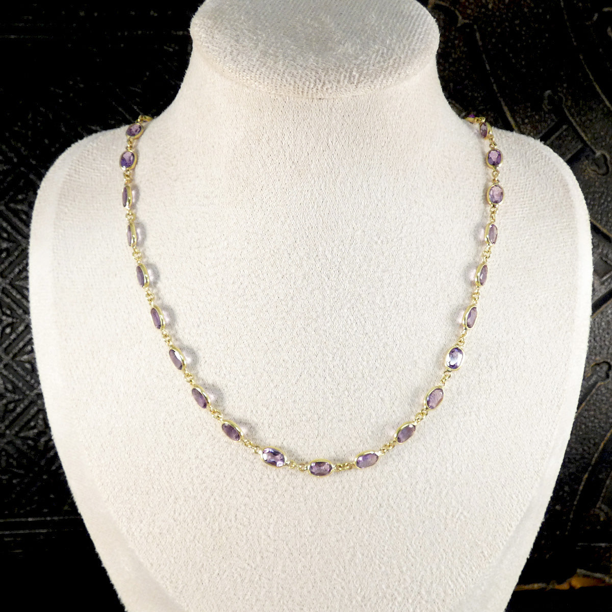 Necklace with purple beads on a mannequin bust against a dark background
