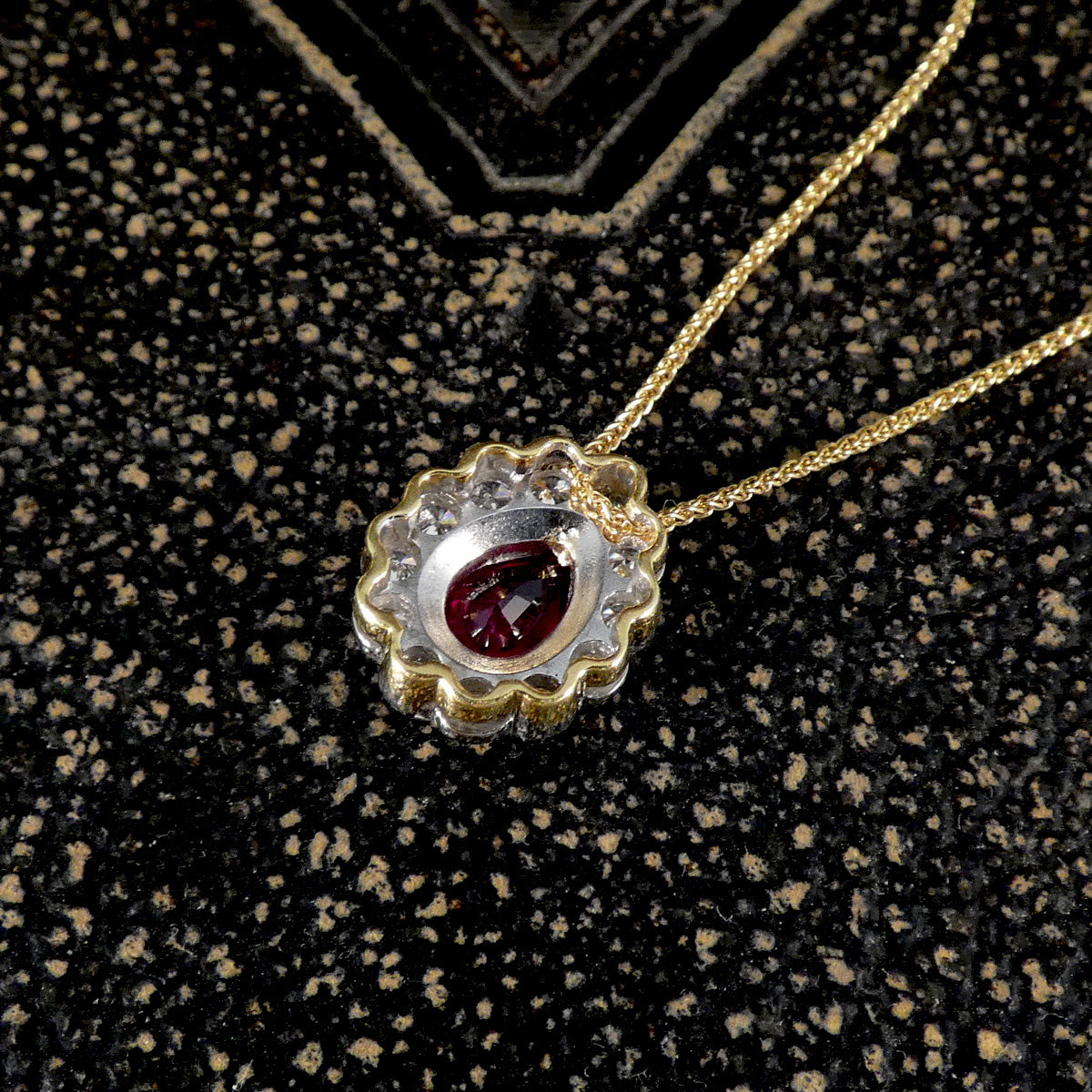 Gold necklace with a pendant featuring a red gemstone on a textured black background